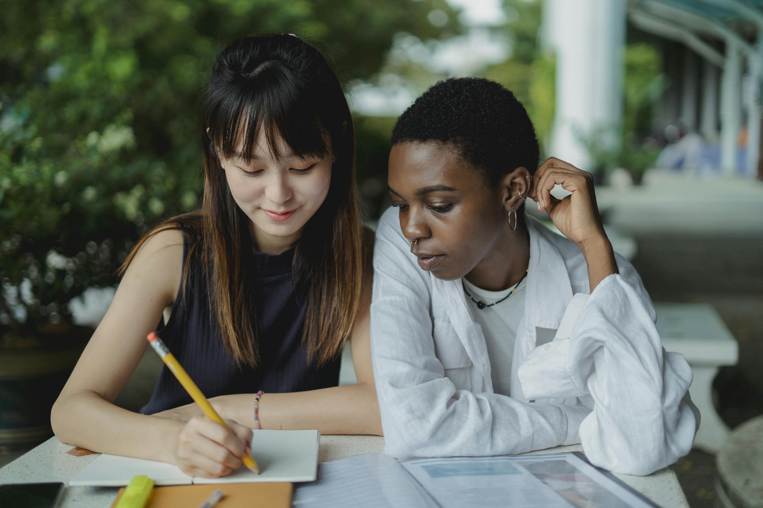 Two women studying together outdoors. A warm display of friendship and collaboration.